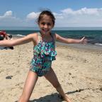 Nine-year-old Josie smiles on the beach on a sunny day.