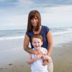 A young boy and his mother stand smiling on a beach.