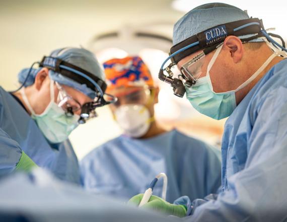 Three surgeons in scrubs performing surgery.