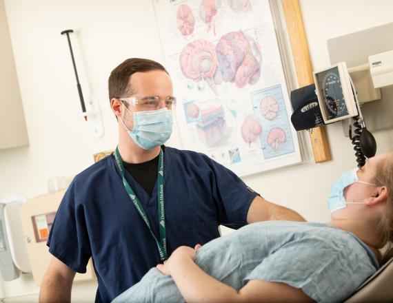 A caregiver speaks with a patient. On the wall hangs a poster of the anatomy of the brain.