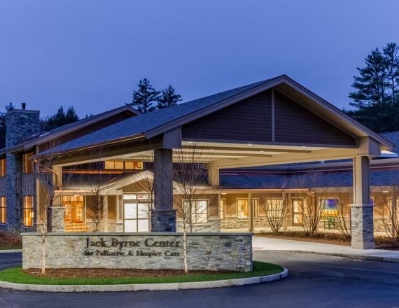 Exterior photo of the Jack Byrne Center for Palliative & Hospice Care, aglow in the twilight. 