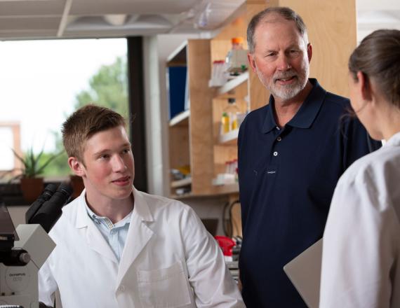 A young investigator sits in front of a microscope with his mentor by his side.