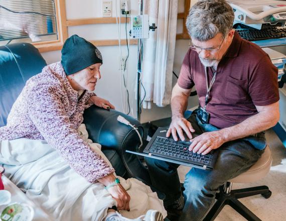 Marv Klassen-Landis, a member of Dartmouth-Hitchcock’s creative arts team, types on a laptop as a patient looks on.