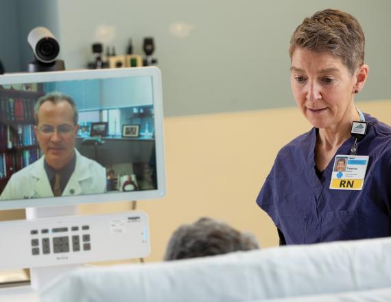 Keith McAvoy, MD, medical director of the teleNeurology service and section chief of general neurology at Dartmouth Hitchcock Clinics Manchester (shown on screen) consults with a bedside clinician and a patient via a telehealth cart. (Photo taken prior to COVID-19 protocols.)