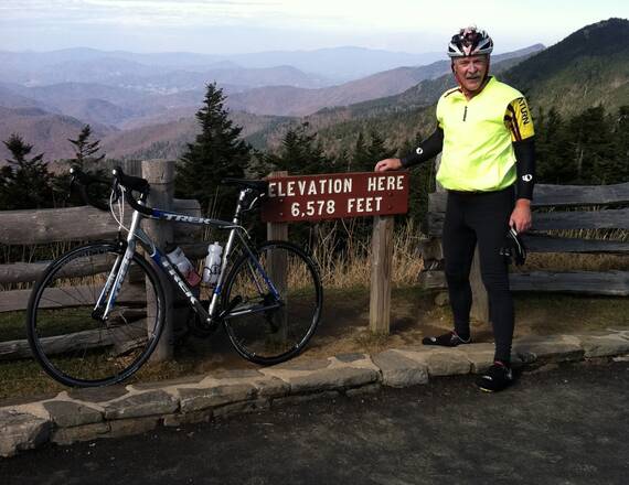 Larry Morgan, an avid cyclist and pacemaker patient, stands next to his bike and a sign that says, "elevation here 6,578 feet."