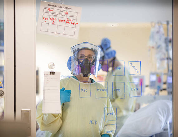 healthcare worker in protective gear standing behind a glass wall