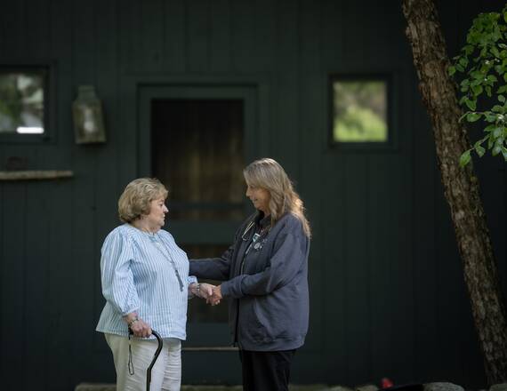 A home health provider holds the hand of a patient using a cane outside her home