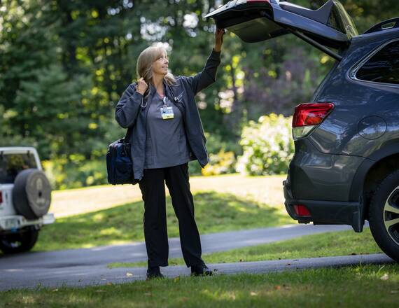 A home health nurse closes her car's trunk before heading to a patient visit