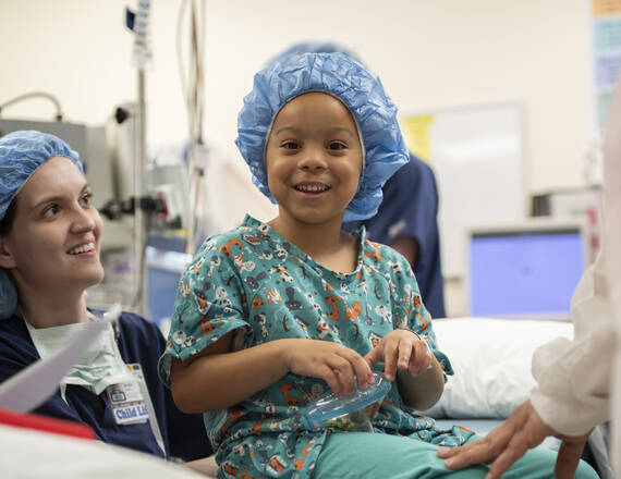 A young boy sitting on an exam bed smiling with a health provider smiling behind him