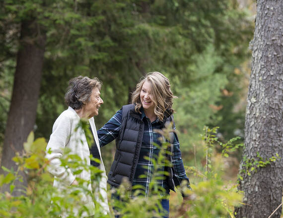 An older woman walks with a younger woman in the forest