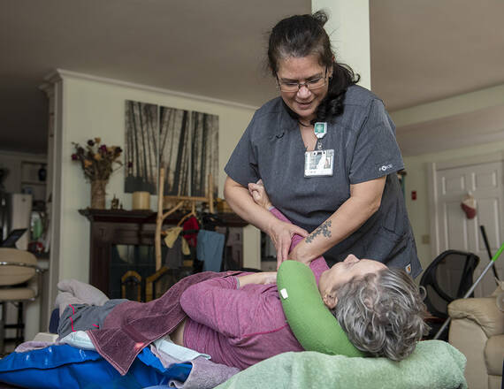 A female home health care aide assists a woman in her bed.